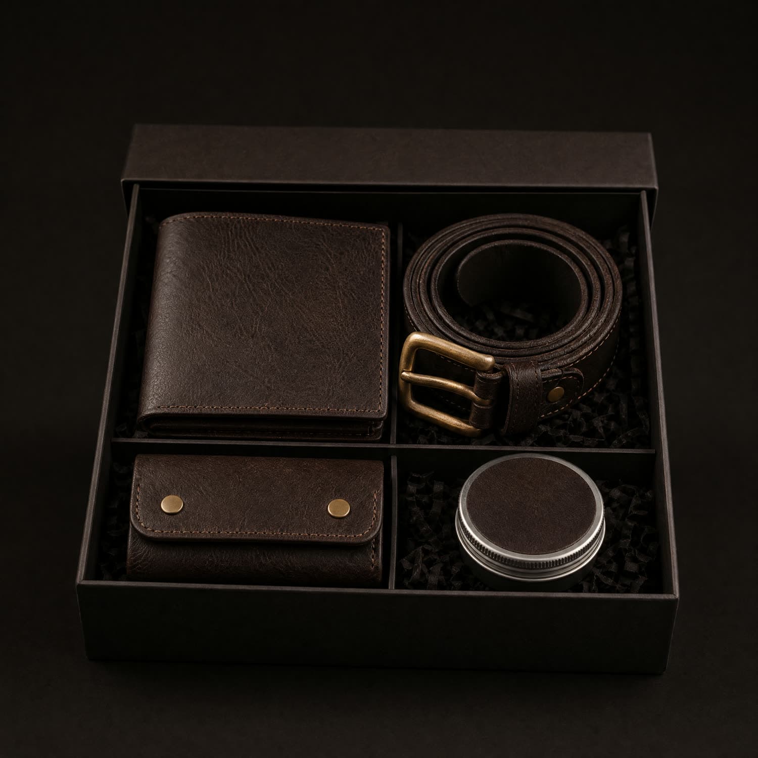 Four matched espresso leather items in an open presentation box: a bifold wallet, a coiled belt, a key case and a balm tin